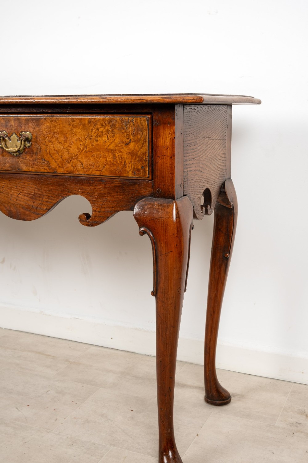A Queen Anne style burr walnut console table featuring two drawers, a shaped apron, and four slender cabriole legs terminating in pad feet. View VI