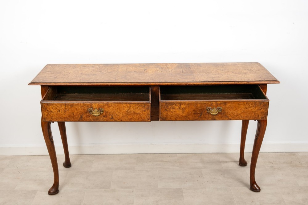 A Queen Anne style burr walnut console table featuring two drawers, a shaped apron, and four slender cabriole legs terminating in pad feet. View VII