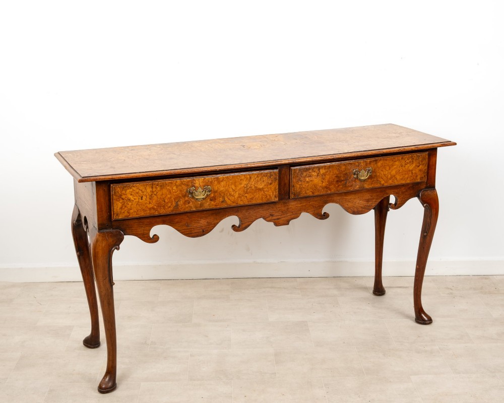 A Queen Anne style burr walnut console table featuring two drawers, a shaped apron, and four slender cabriole legs terminating in pad feet. View VIII