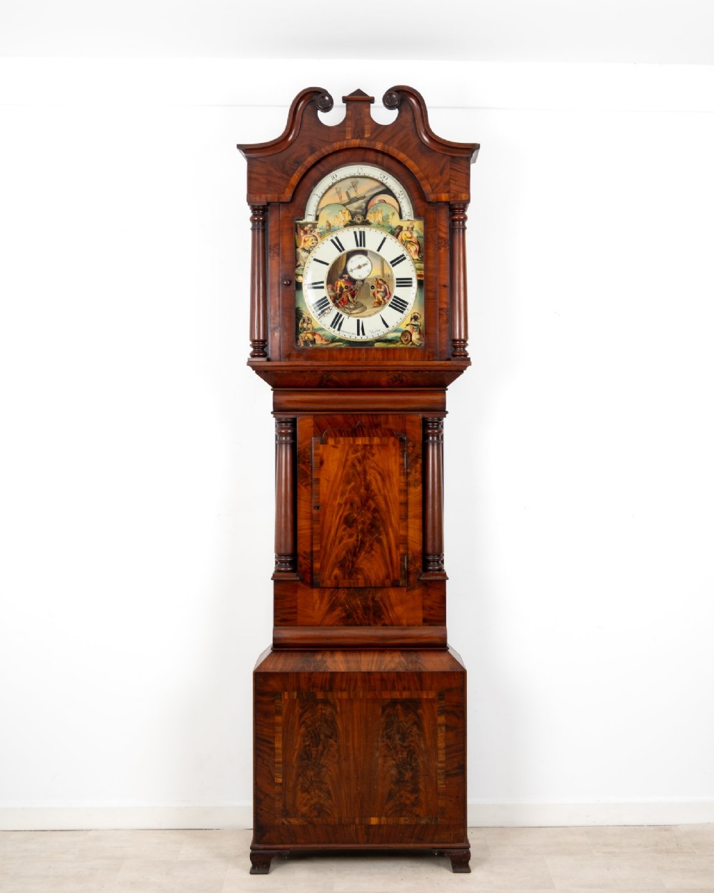 An antique mahogany longcase clock featuring a swan-neck pediment, turned columns, and a hand-painted arch dial with a moon phase display. View II