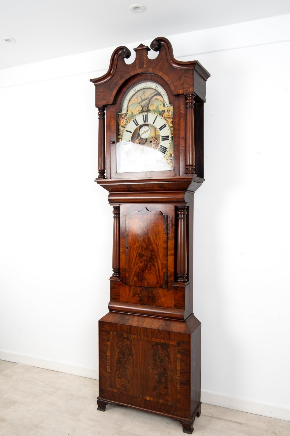 An antique mahogany longcase clock featuring a swan-neck pediment, turned columns, and a hand-painted arch dial with a moon phase display. View V
