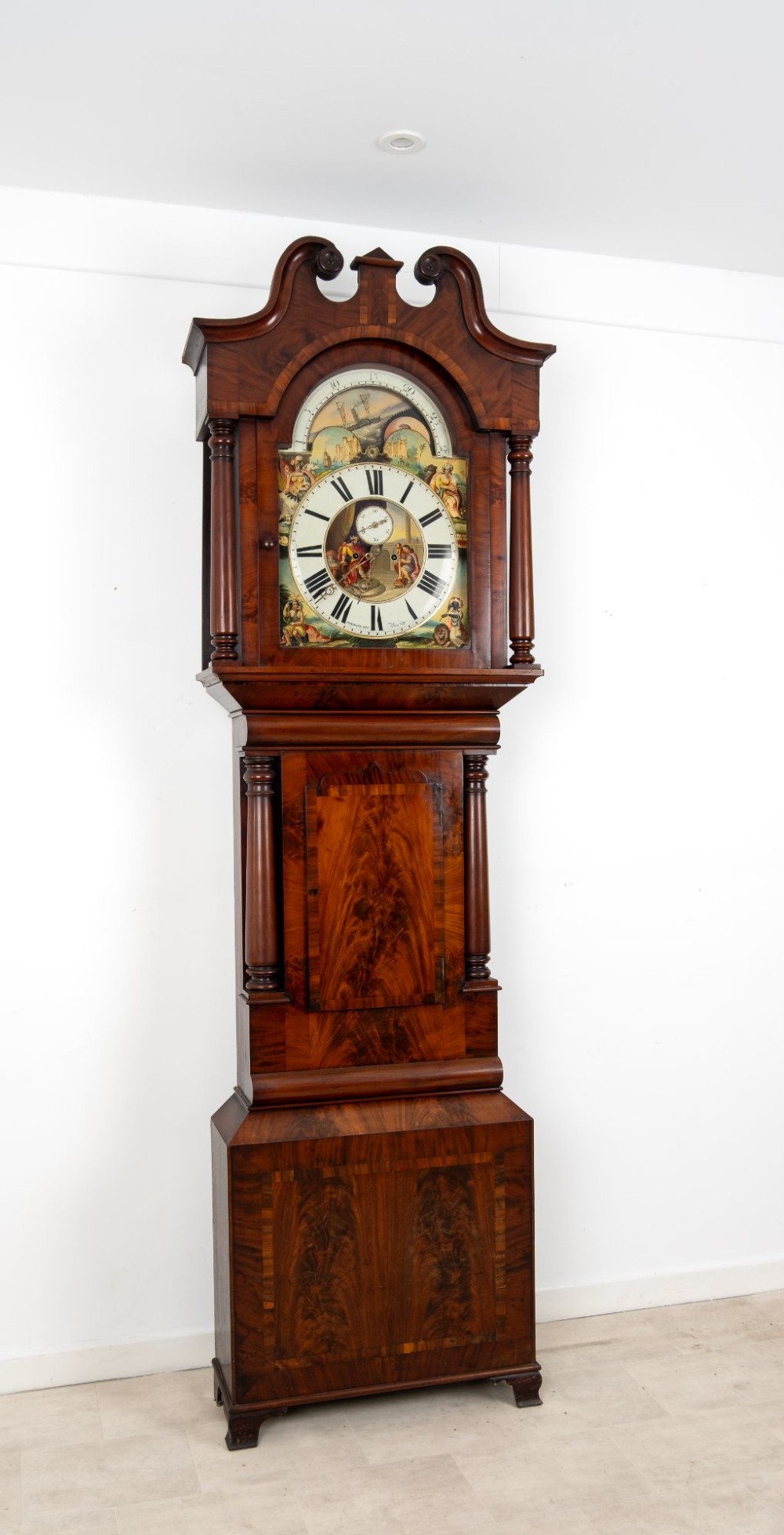 An antique mahogany longcase clock featuring a swan-neck pediment, turned columns, and a hand-painted arch dial with a moon phase display. View VI