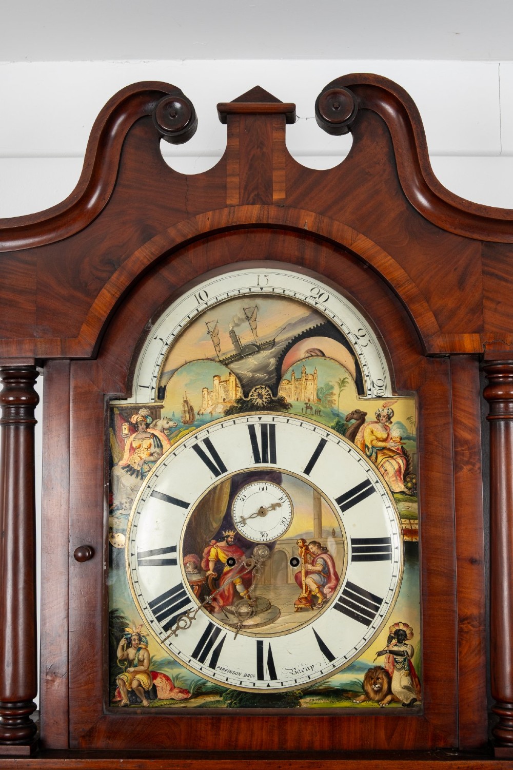 An antique mahogany longcase clock featuring a swan-neck pediment, turned columns, and a hand-painted arch dial with a moon phase display. View VII