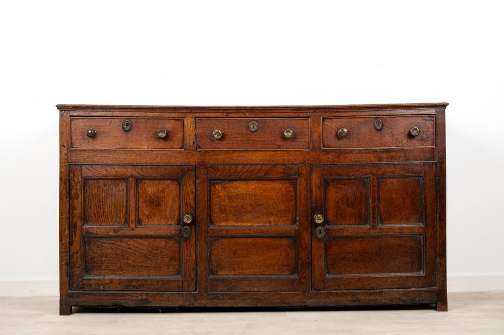 A Georgian antique oak dresser base featuring three upper drawers with metal keyhole escutcheons above three panelled cupboard doors.