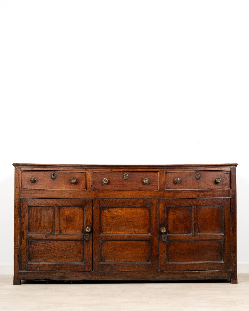 A Georgian antique oak dresser base featuring three upper drawers with metal keyhole escutcheons above three panelled cupboard doors. View II