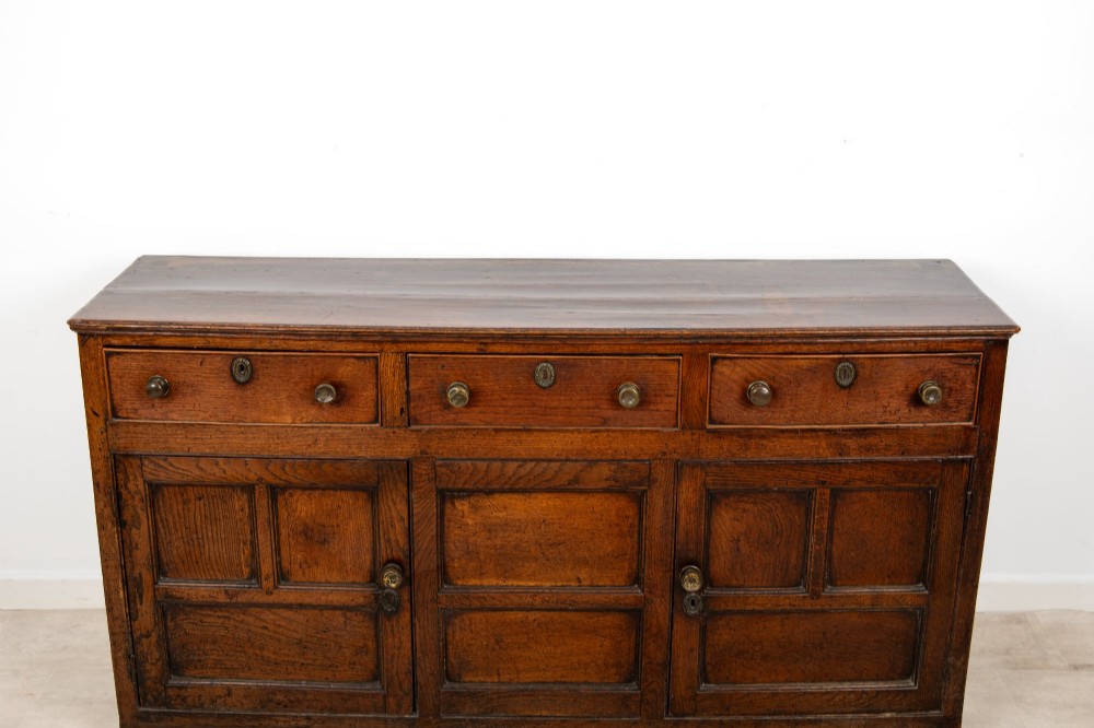 A Georgian antique oak dresser base featuring three upper drawers with metal keyhole escutcheons above three panelled cupboard doors. View V