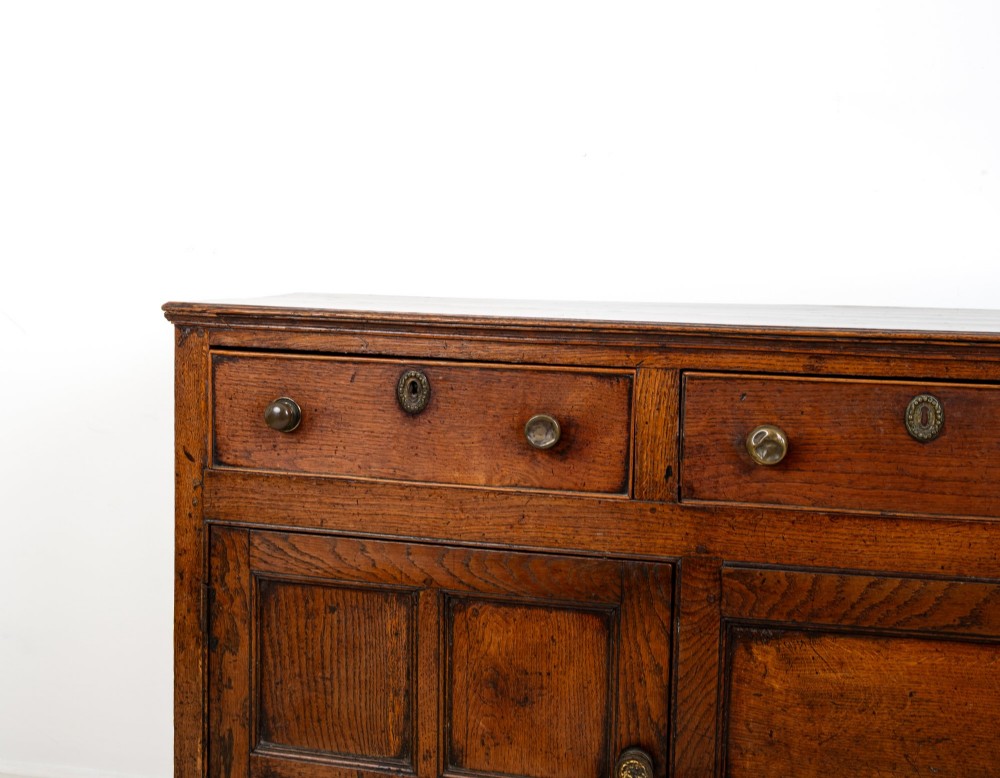 A Georgian antique oak dresser base featuring three upper drawers with metal keyhole escutcheons above three panelled cupboard doors. View VI