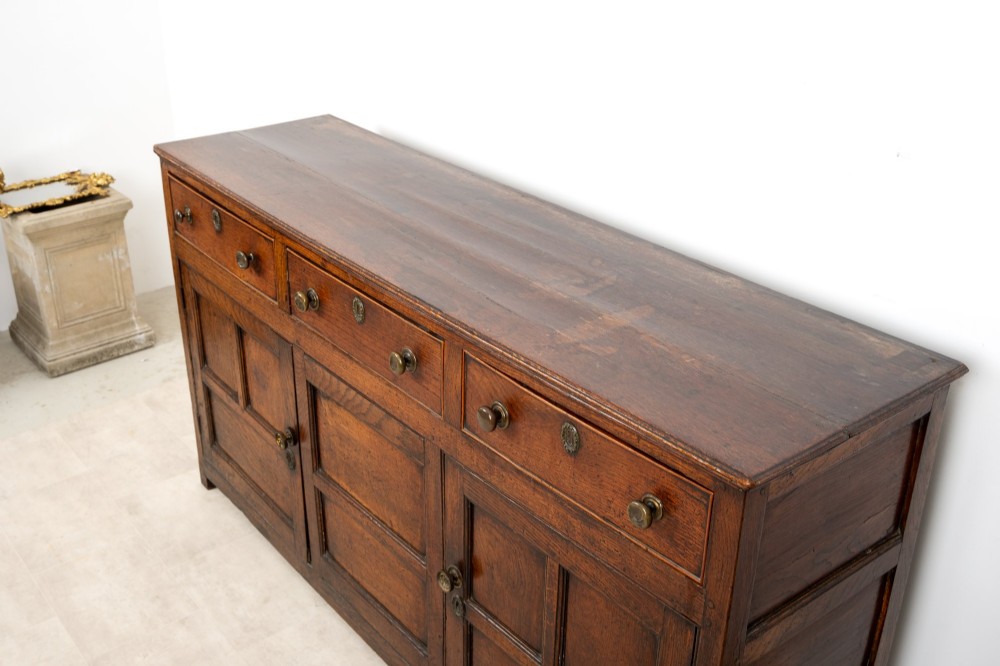A Georgian antique oak dresser base featuring three upper drawers with metal keyhole escutcheons above three panelled cupboard doors. View VIII