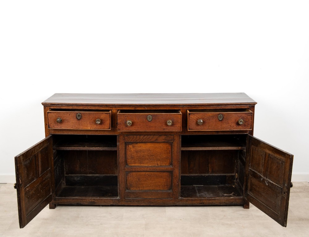 A Georgian antique oak dresser base featuring three upper drawers with metal keyhole escutcheons above three panelled cupboard doors. View IX