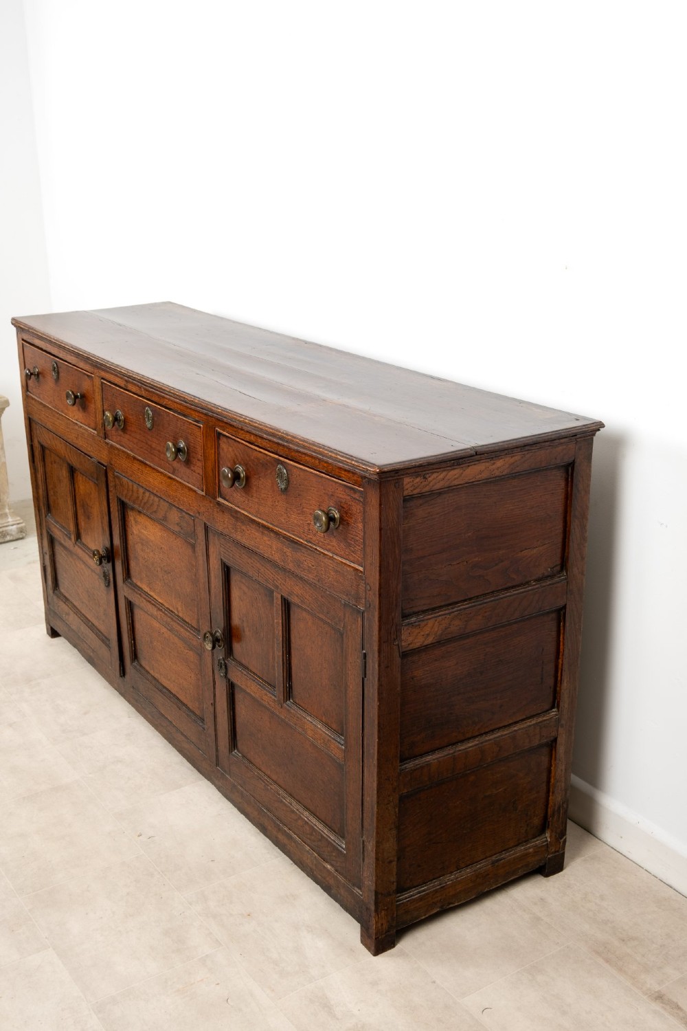 A Georgian antique oak dresser base featuring three upper drawers with metal keyhole escutcheons above three panelled cupboard doors. View X