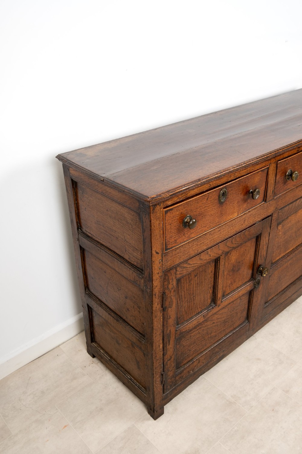A Georgian antique oak dresser base featuring three upper drawers with metal keyhole escutcheons above three panelled cupboard doors. View XI