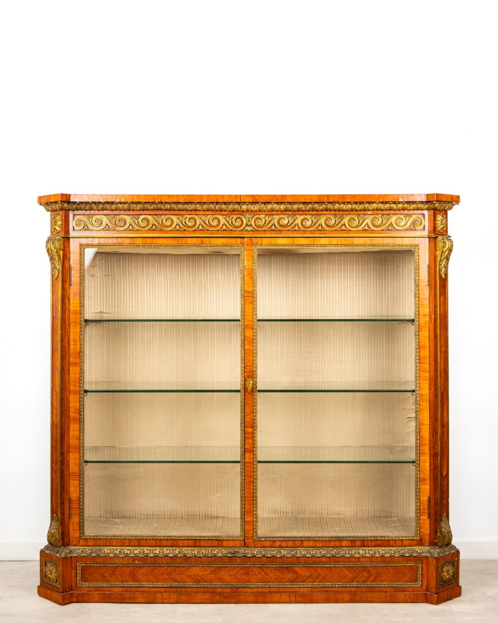 A large veneered display cabinet featuring gilt-bronze mounts, glazed twin doors, glass shelving, and a fabric-lined interior. View II