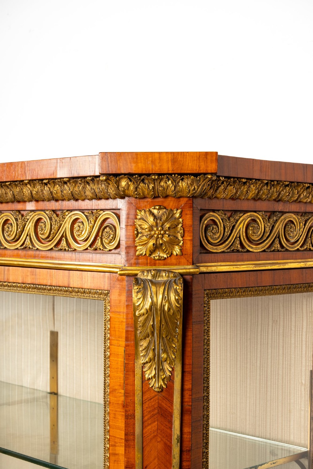 A large veneered display cabinet featuring gilt-bronze mounts, glazed twin doors, glass shelving, and a fabric-lined interior. View V