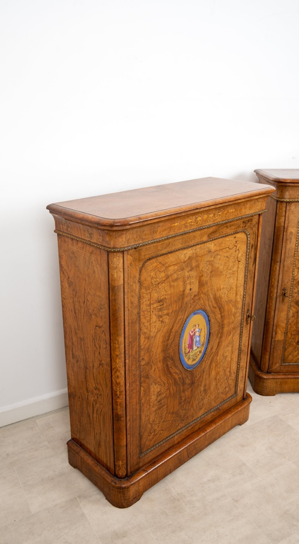 A pair of Victorian burr walnut side cabinets featuring inlaid boxwood detailing, gilt metal trim, and central oval blue porcelain plaques painted with classical figures. View IX
