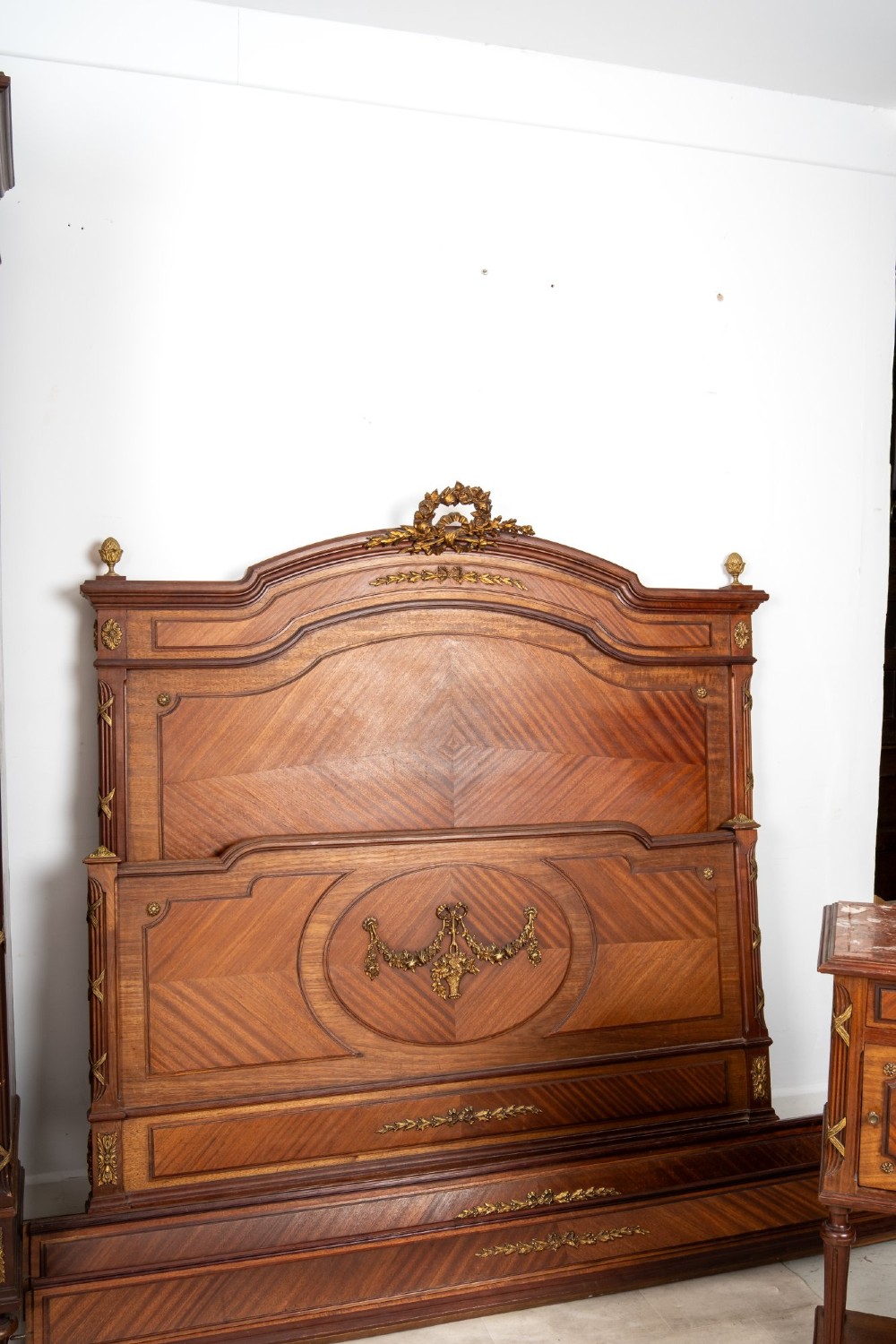 A French Louis XVI Revival mahogany bedroom suite comprising a mirrored two-door armoire, a matching bedframe with parquetry detailing, and a marble-topped bedside table with gilded bronze mounts. View VI