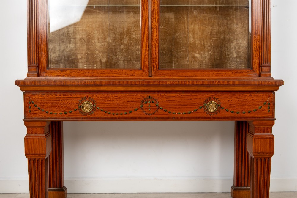 An antique Edwardian painted satinwood display cabinet featuring two glazed doors, glass shelves, fluted tapering legs, and classical hand-painted figurative and floral panels. View III