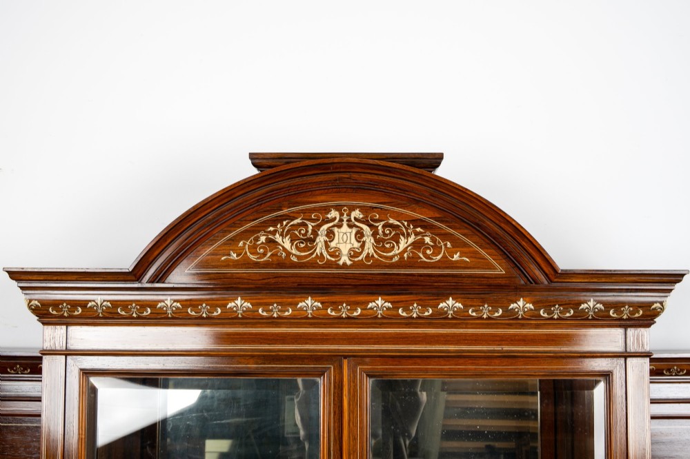 A large late Victorian rosewood display cabinet featuring intricate inlay work, glazed upper and lower doors, an arched pediment, and mirrored back panels. View VII