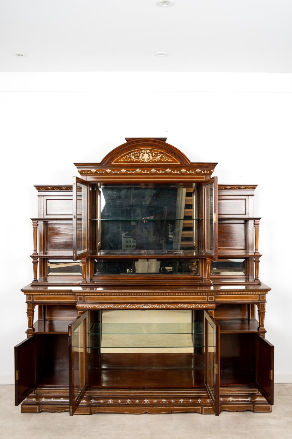A large late Victorian rosewood display cabinet featuring intricate inlay work, glazed upper and lower doors, an arched pediment, and mirrored back panels. View IX