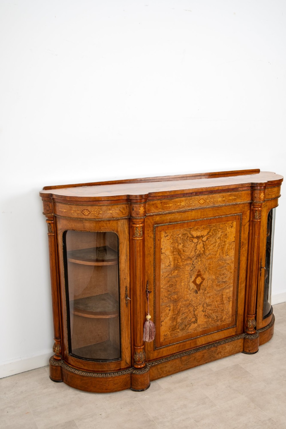 An antique Victorian burr walnut credenza featuring a central inlaid marquetry door flanked by two curved glazed display cabinets and gilt mounts. View VI