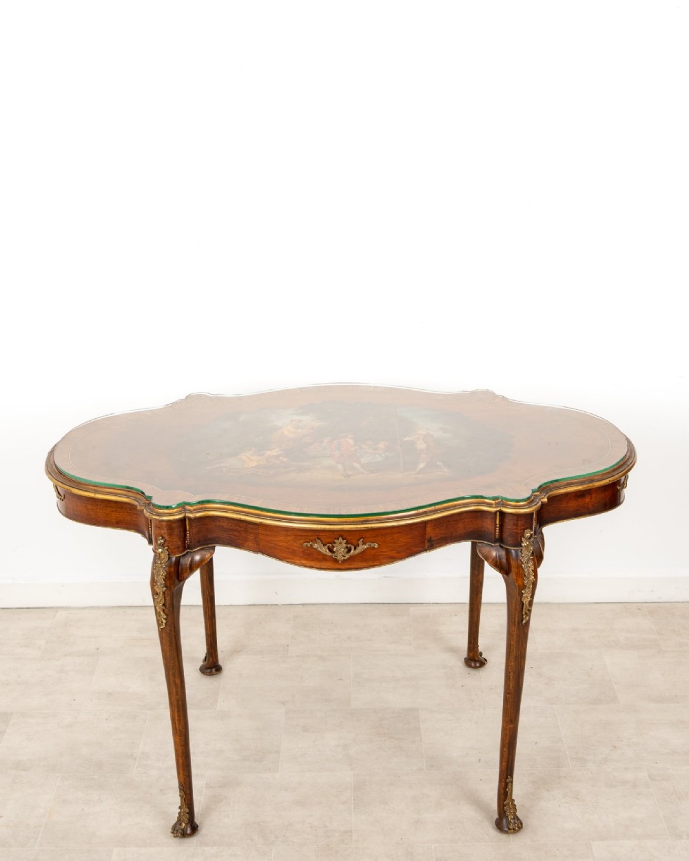 A French Louis XV style centre table featuring a serpentine glass-covered top with a painted figurative scene, cabriole legs, and ornate gilt bronze mounts.