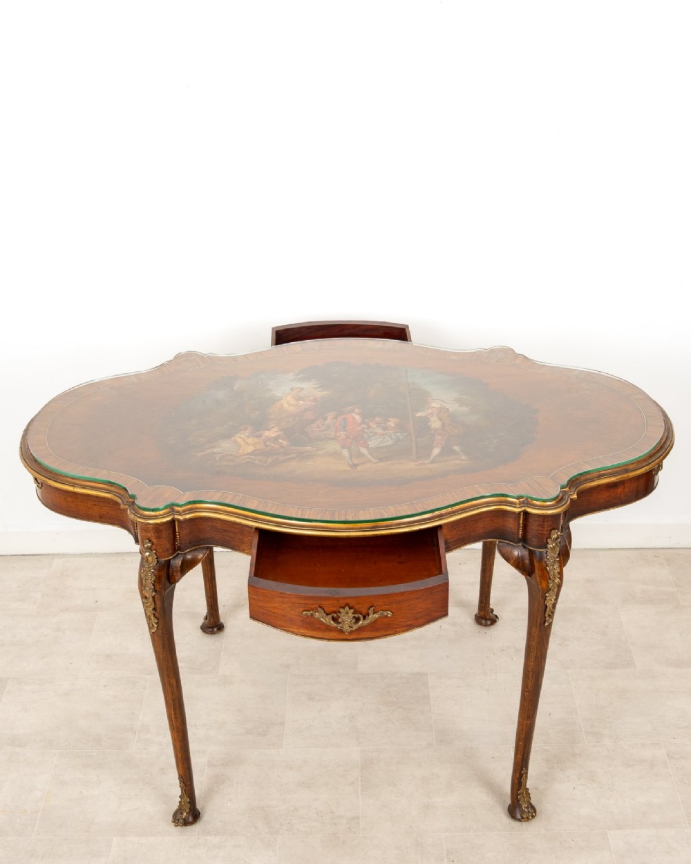 A French Louis XV style centre table featuring a serpentine glass-covered top with a painted figurative scene, cabriole legs, and ornate gilt bronze mounts. View V