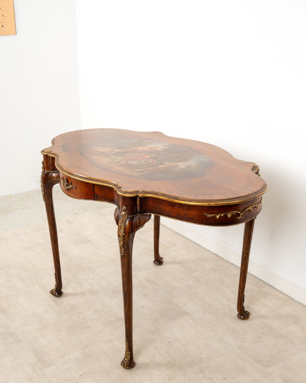A French Louis XV style centre table featuring a serpentine glass-covered top with a painted figurative scene, cabriole legs, and ornate gilt bronze mounts. View VII