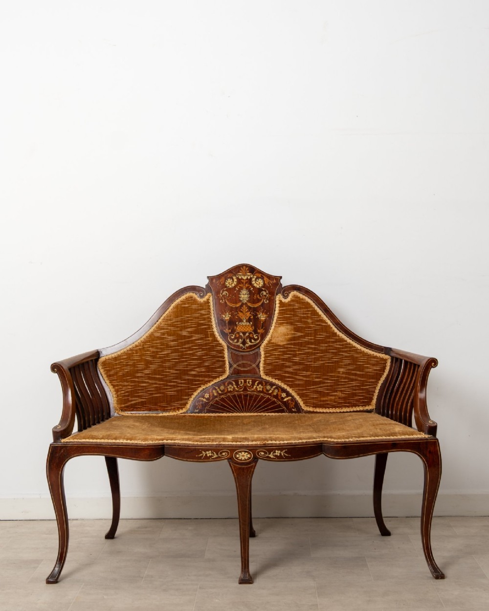 An Edwardian mahogany settee featuring floral marquetry inlay on a central back panel, slatted arms, cabriole legs, and gold-brown velvet upholstery.