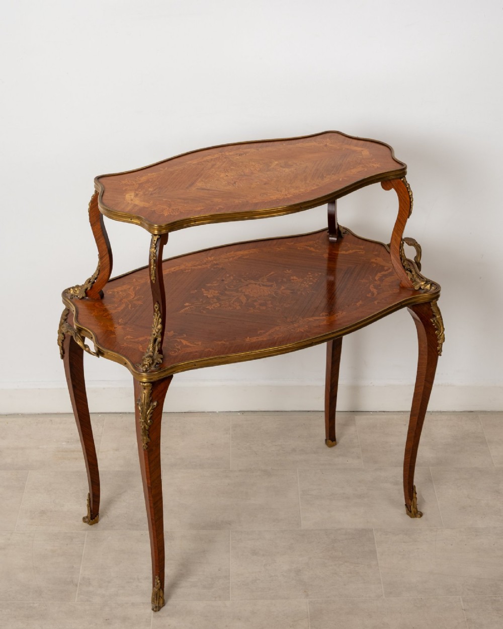 An antique Louis XV style two-tier kingwood side table featuring floral marquetry inlay, serpentine edges, and gilt-bronze mounts on cabriole legs.