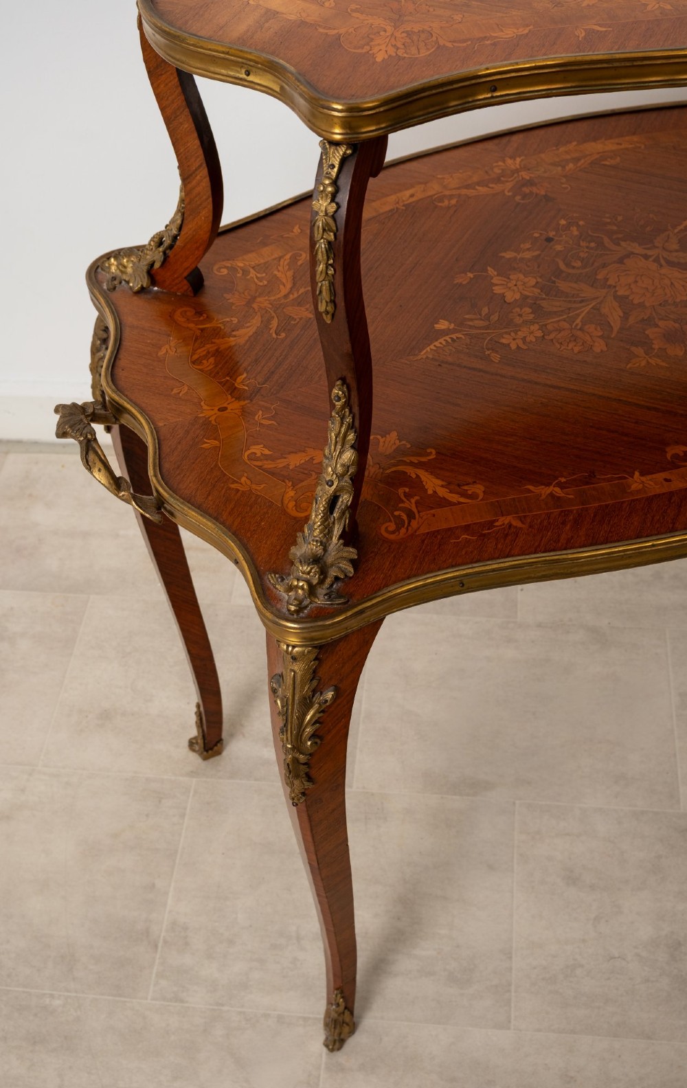 An antique Louis XV style two-tier kingwood side table featuring floral marquetry inlay, serpentine edges, and gilt-bronze mounts on cabriole legs. View VI