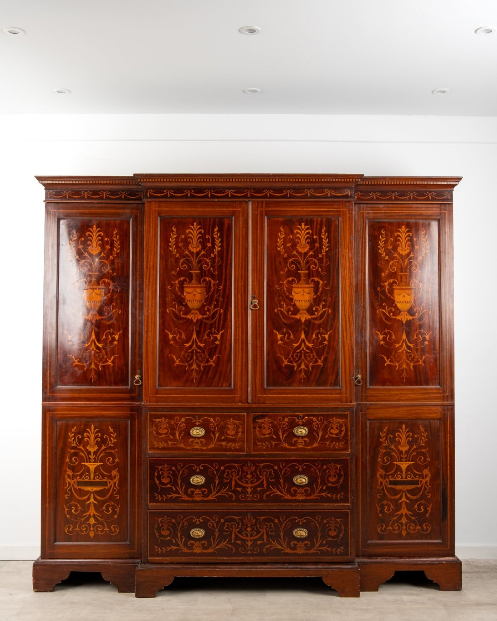 An Edwardian mahogany compactum wardrobe featuring classical urn marquetry inlay, side hanging sections, central drawers, and panelled cupboard doors.