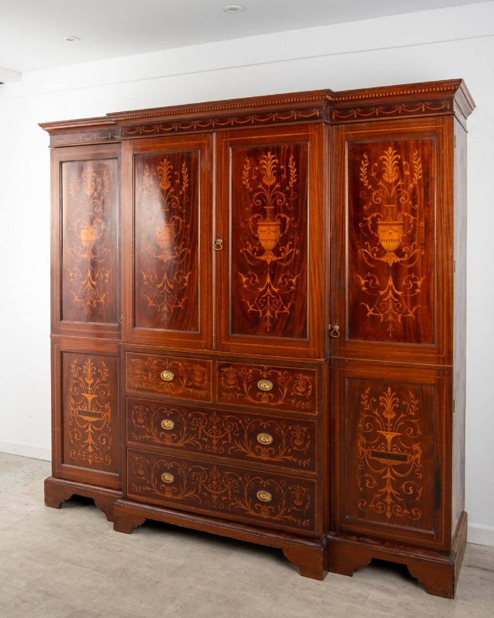 An Edwardian mahogany compactum wardrobe featuring classical urn marquetry inlay, side hanging sections, central drawers, and panelled cupboard doors. View III