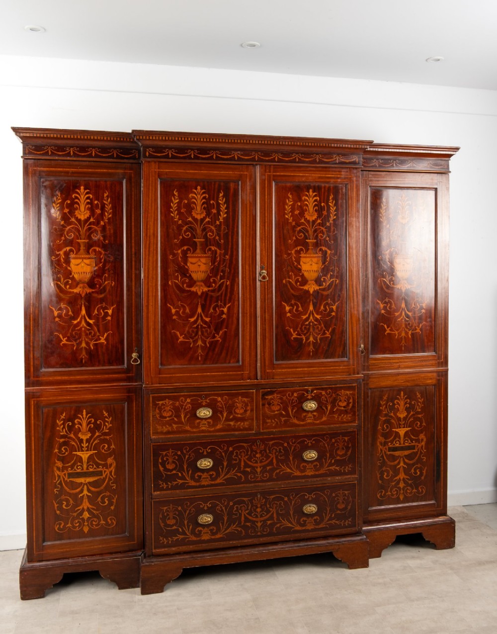 An Edwardian mahogany compactum wardrobe featuring classical urn marquetry inlay, side hanging sections, central drawers, and panelled cupboard doors. View IV