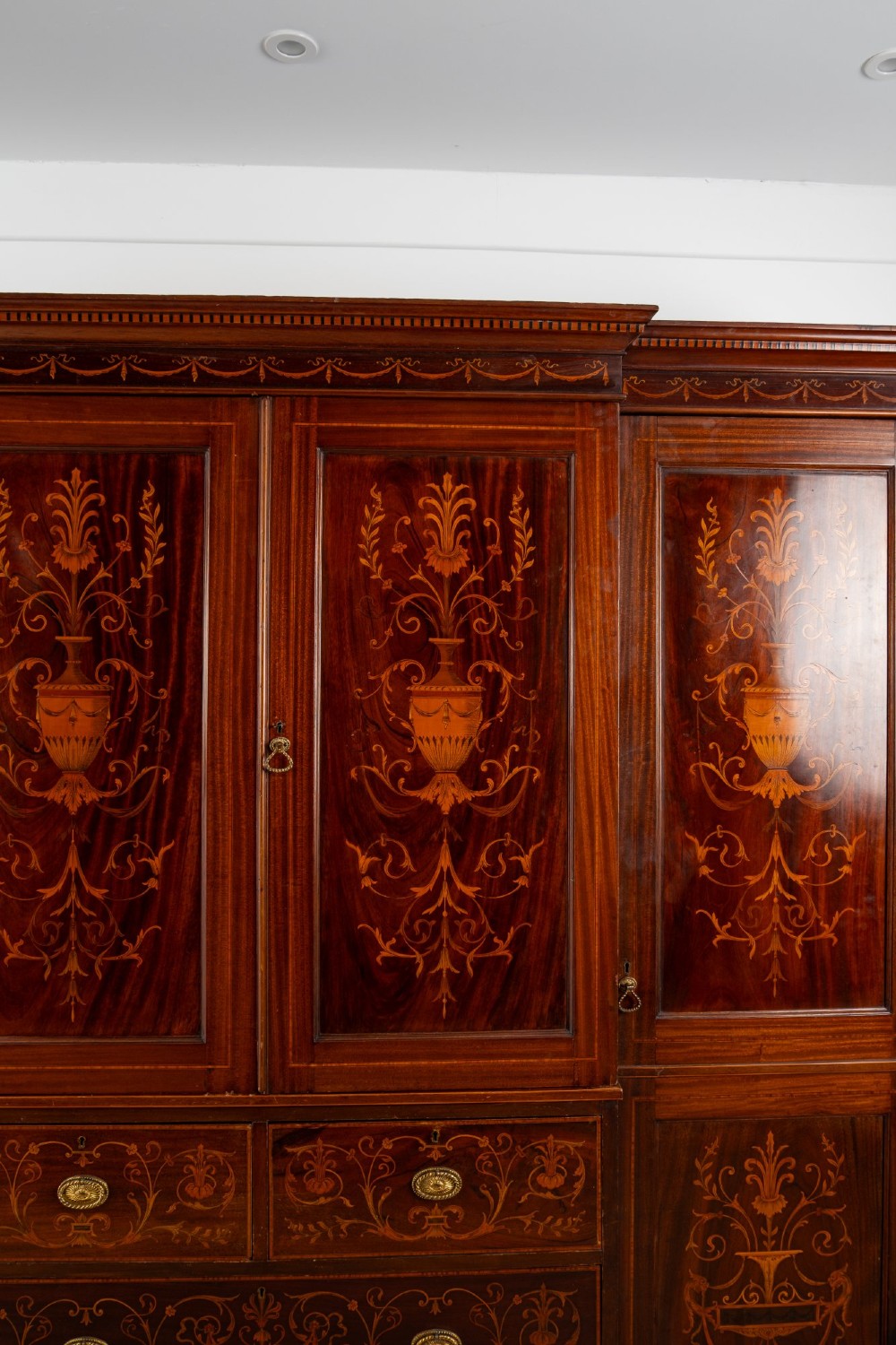 An Edwardian mahogany compactum wardrobe featuring classical urn marquetry inlay, side hanging sections, central drawers, and panelled cupboard doors. View V