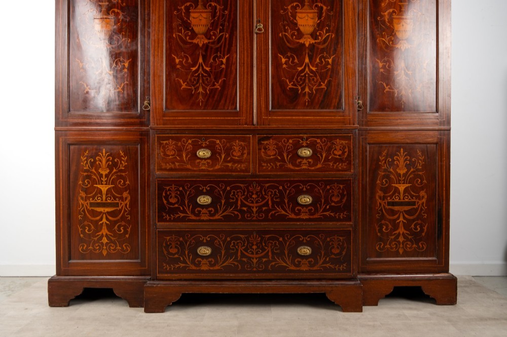 An Edwardian mahogany compactum wardrobe featuring classical urn marquetry inlay, side hanging sections, central drawers, and panelled cupboard doors. View VI