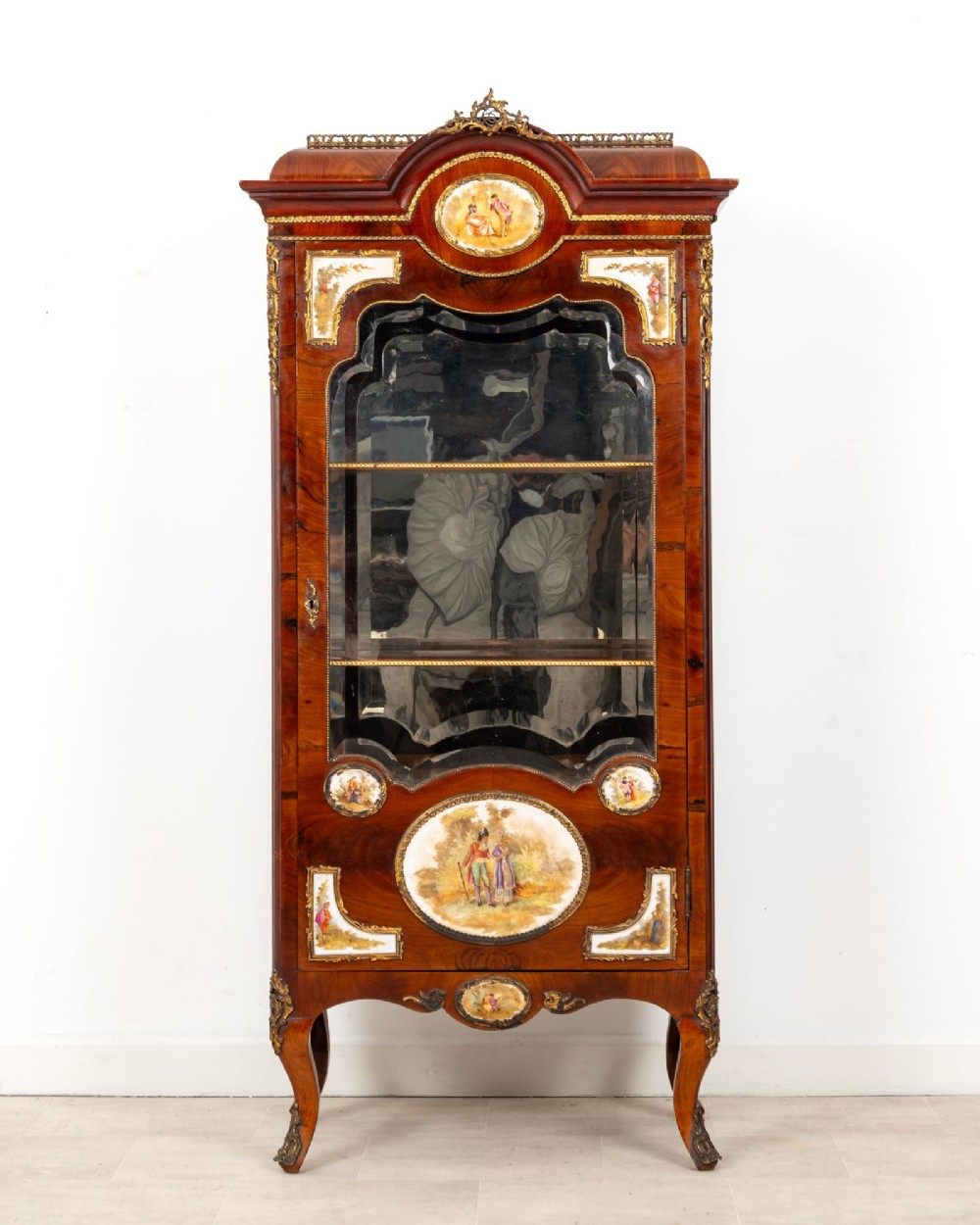 An antique French walnut vitrine featuring a single glass door, hand-painted porcelain plaques, gilt-bronze ormolu mounts, and cabriole legs.