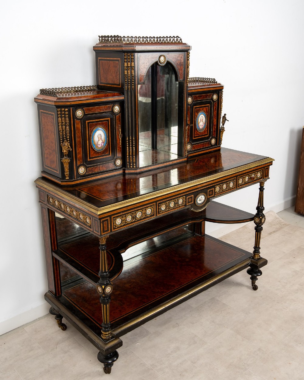 A nineteenth-century French ebonised and amboyna bonheur du jour desk featuring porcelain plaques, mirrored panels, turned legs, and brass mounts. View V