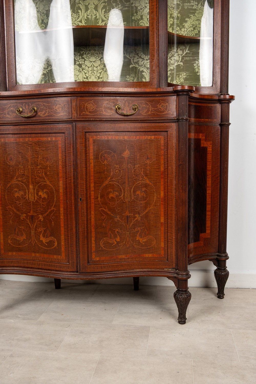 An Edwardian mahogany display cabinet featuring satinwood marquetry inlay, glazed upper doors with green fabric lining, and turned legs. View III