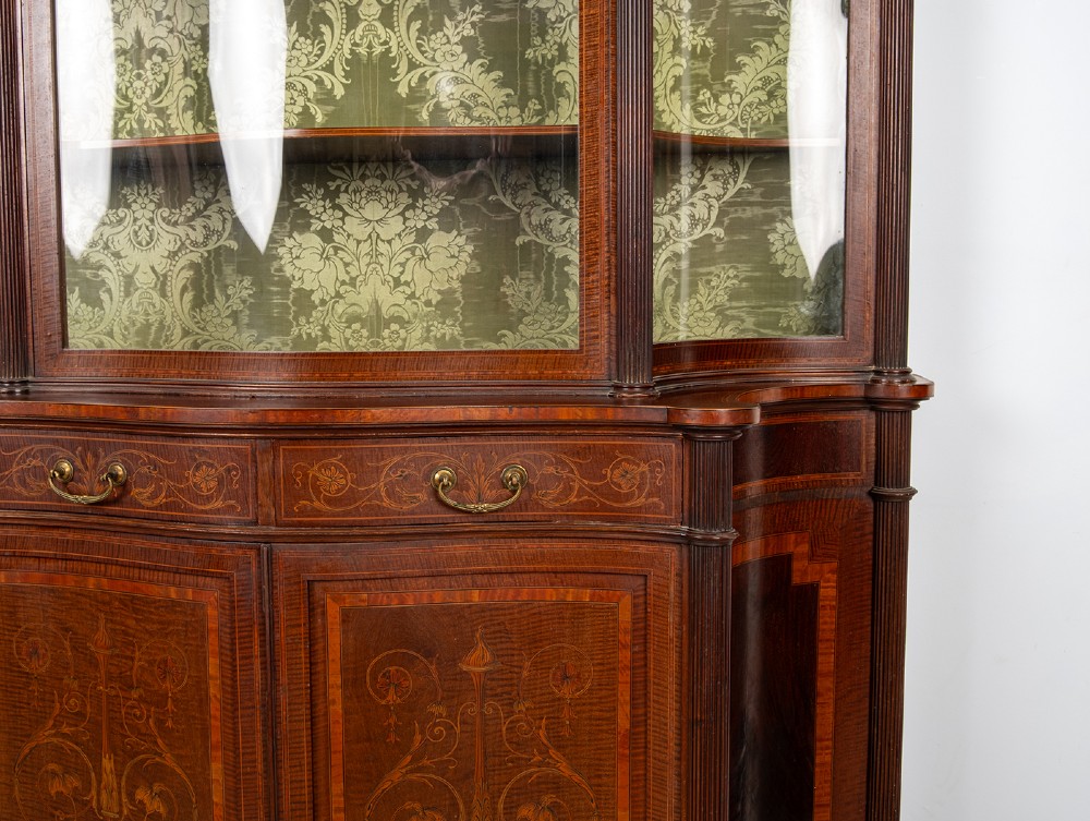 An Edwardian mahogany display cabinet featuring satinwood marquetry inlay, glazed upper doors with green fabric lining, and turned legs. View IV
