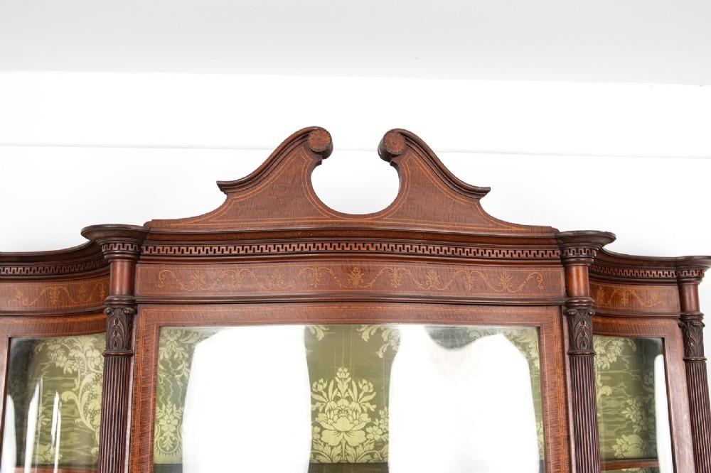 An Edwardian mahogany display cabinet featuring satinwood marquetry inlay, glazed upper doors with green fabric lining, and turned legs. View VI