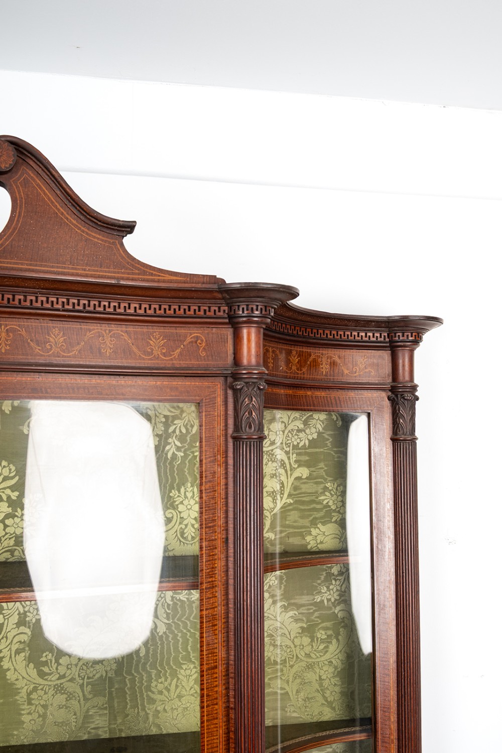 An Edwardian mahogany display cabinet featuring satinwood marquetry inlay, glazed upper doors with green fabric lining, and turned legs. View VII