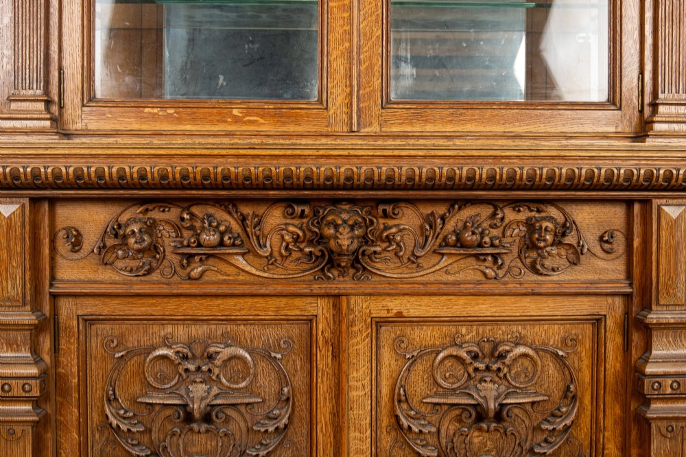 A large Victorian carved oak display cabinet featuring curved glass sides, intricately carved mask motifs on lower door panels, and glass shelving. View XI