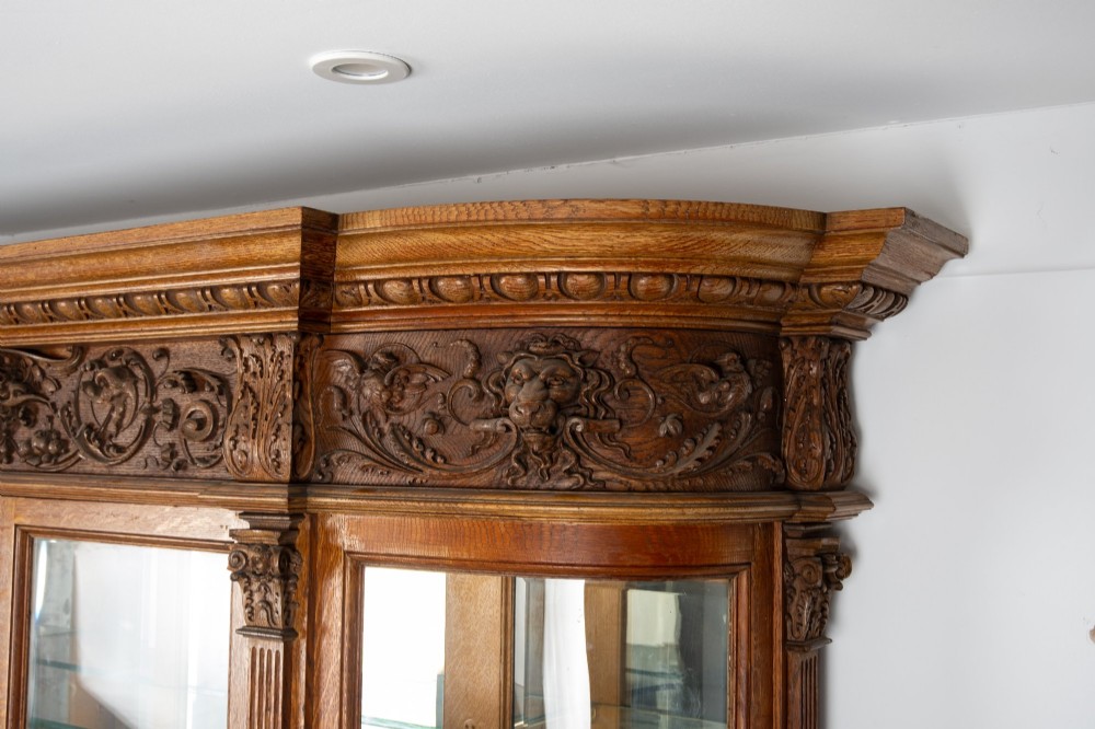 A large Victorian carved oak display cabinet featuring curved glass sides, intricately carved mask motifs on lower door panels, and glass shelving. View XIV