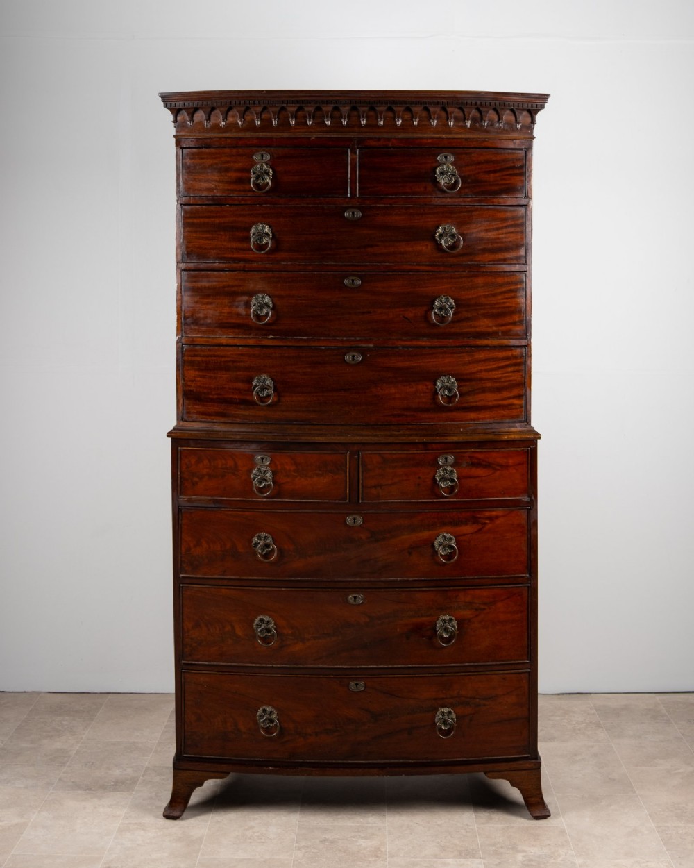 A tall Victorian bow front mahogany chest on chest featuring multiple drawer tiers with brass ring handles and upper cornice trim.