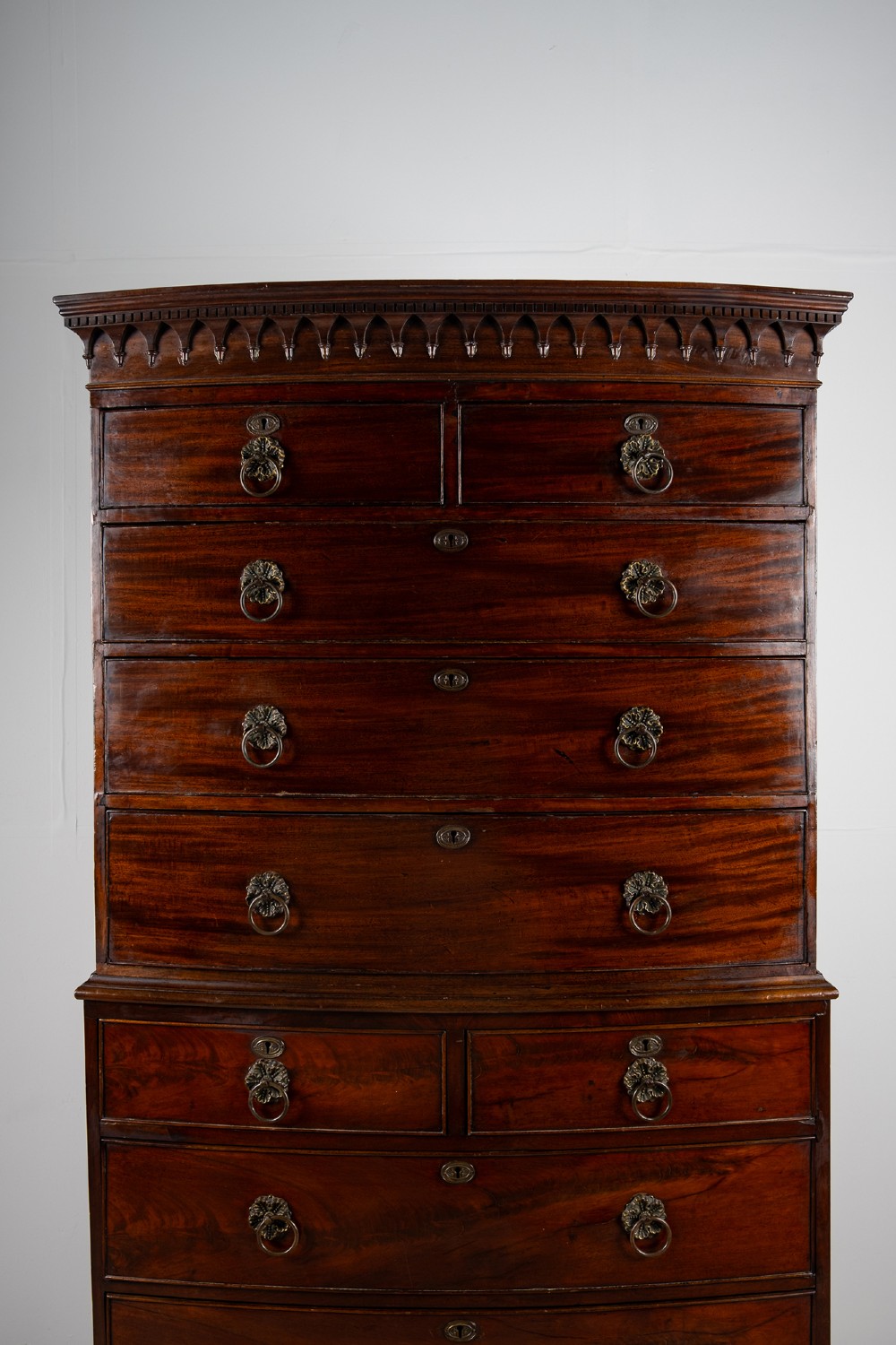 A tall Victorian bow front mahogany chest on chest featuring multiple drawer tiers with brass ring handles and upper cornice trim. View IV