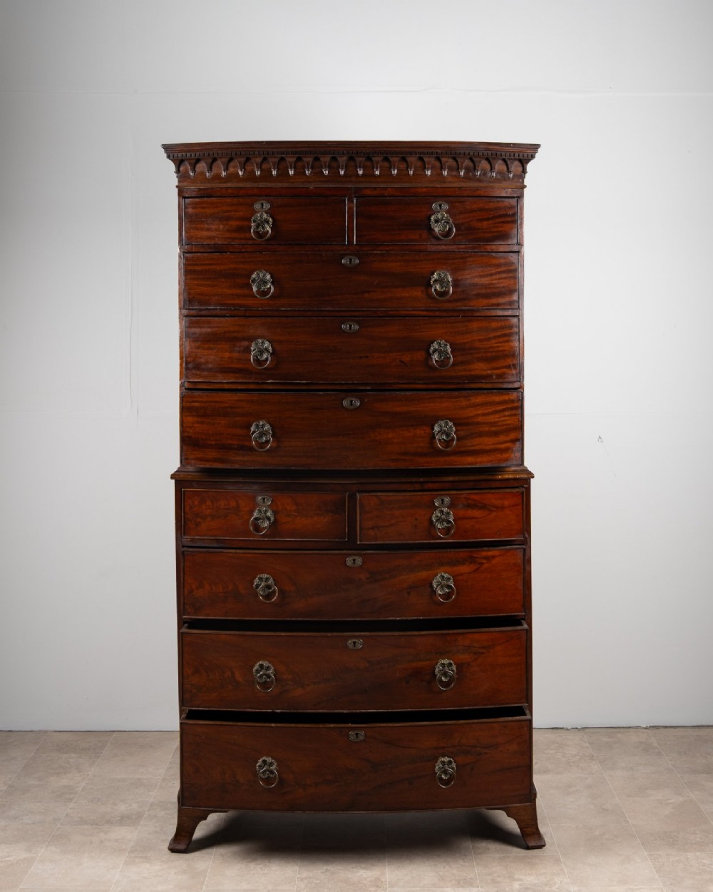 A tall Victorian bow front mahogany chest on chest featuring multiple drawer tiers with brass ring handles and upper cornice trim. View V