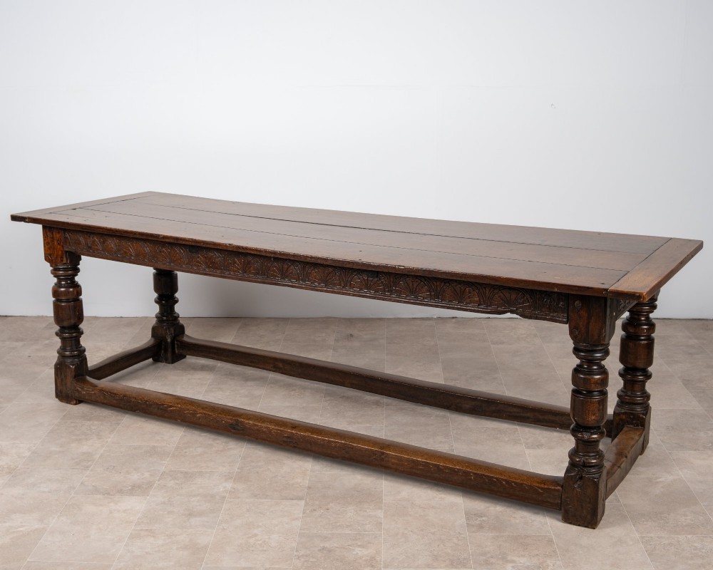 A long 18th-century oak refectory dining table featuring a carved lunette frieze, turned baluster legs, and sturdy box stretchers.