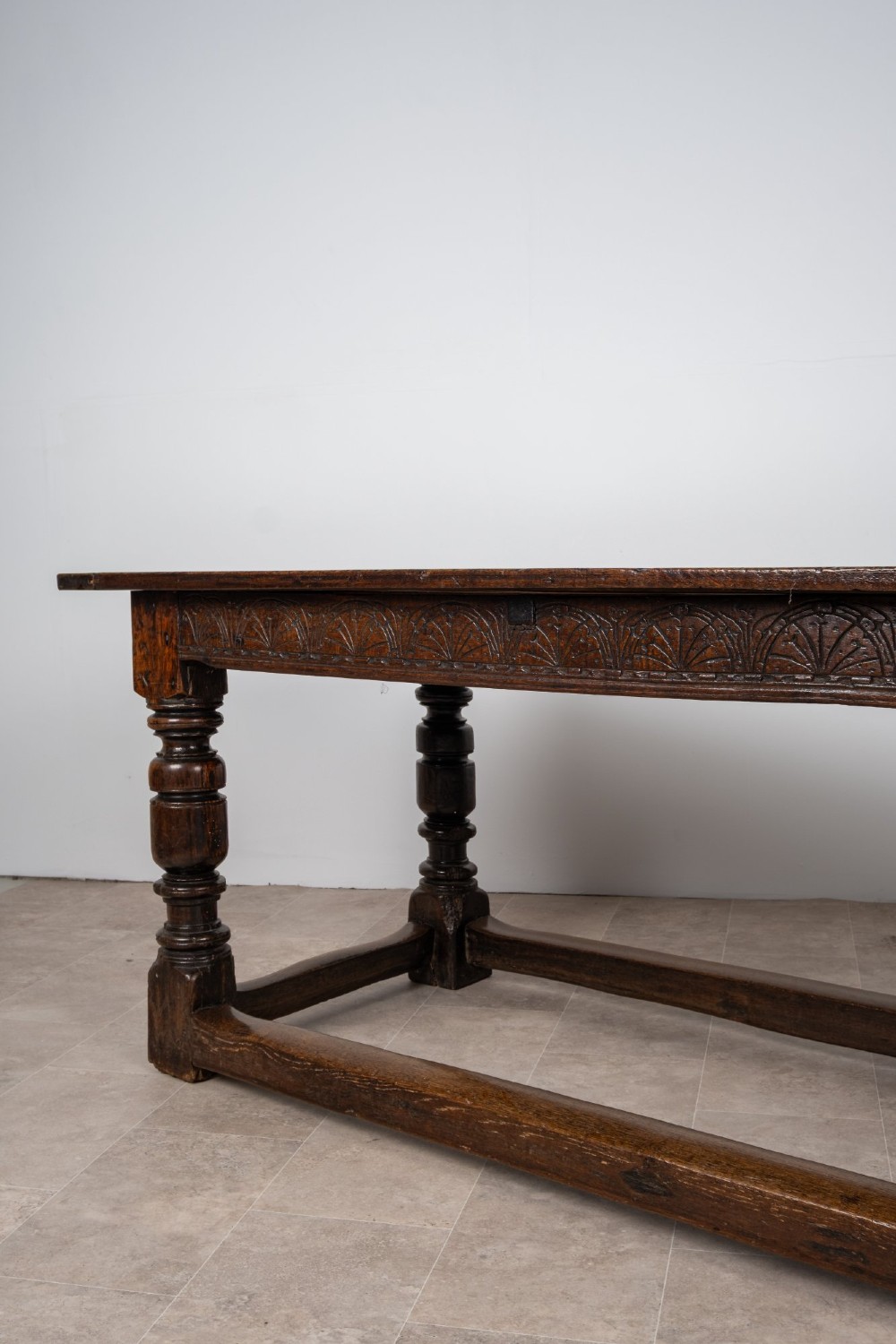 A long 18th-century oak refectory dining table featuring a carved lunette frieze, turned baluster legs, and sturdy box stretchers. View VII