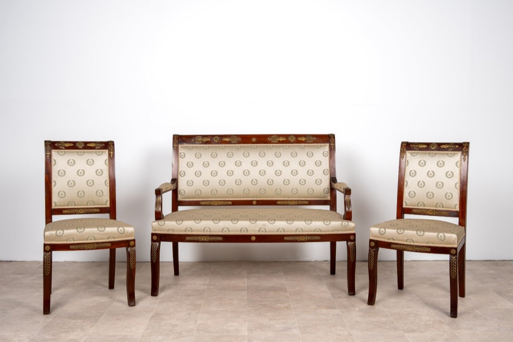 A three-piece antique French Empire Revival salon suite comprising a mahogany two-seater settee and two matching side chairs with gold silk laurel wreath upholstery and ormolu mounts.
