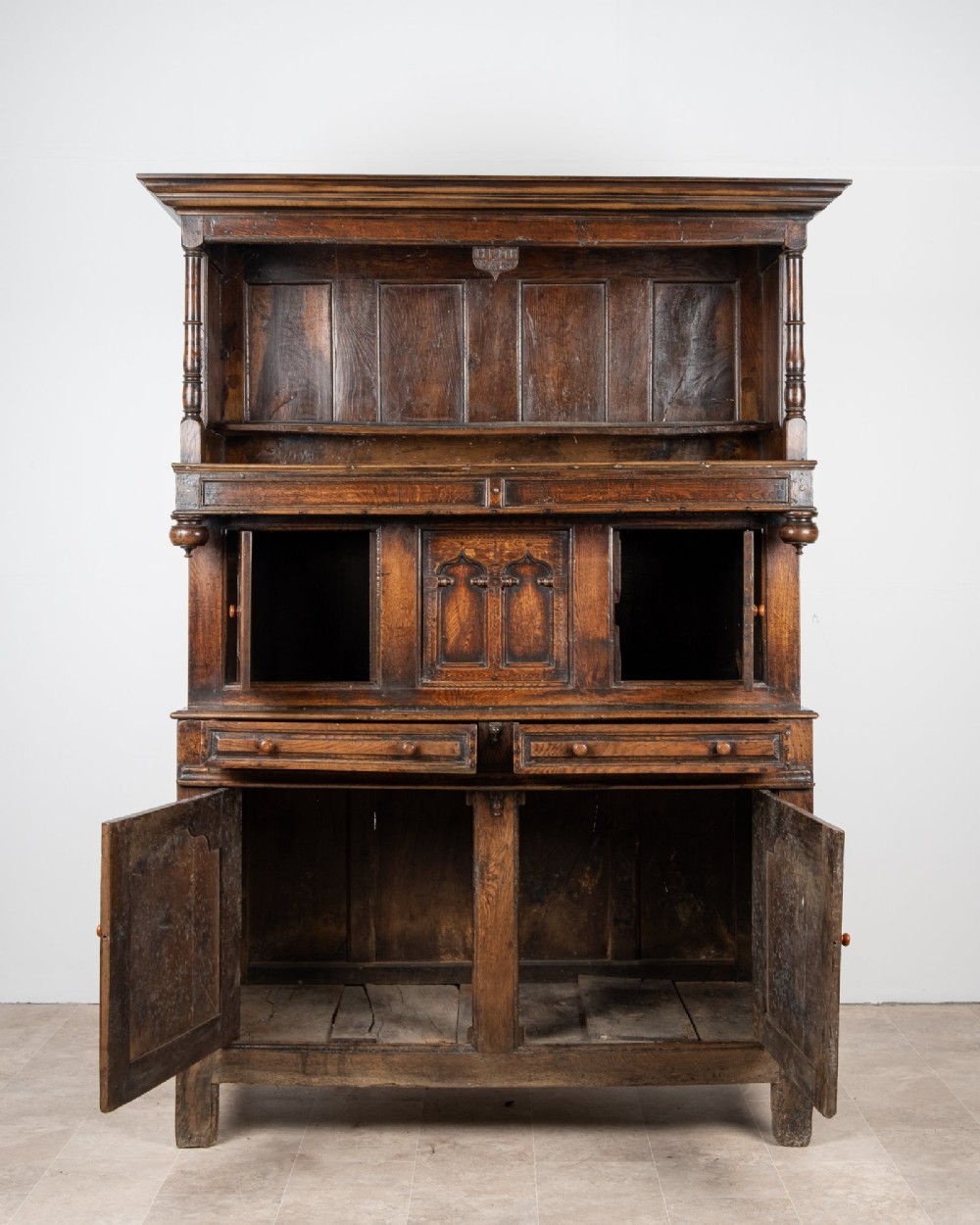 A dark oak three-tier Welsh cwpwrdd tridarn featuring an open upper canopy, middle cupboard section with raised arch panels and turned pillars, and a base cupboard with two drawers. View III