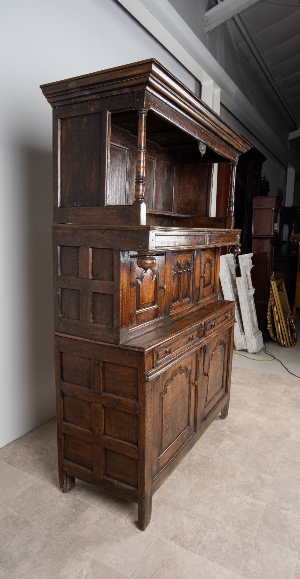 A dark oak three-tier Welsh cwpwrdd tridarn featuring an open upper canopy, middle cupboard section with raised arch panels and turned pillars, and a base cupboard with two drawers. View VII